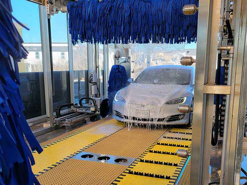 White car driving in ModBrite car wash on belt conveyors