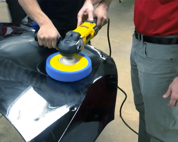 man working on buffing a piece of a vehicle with another person helping